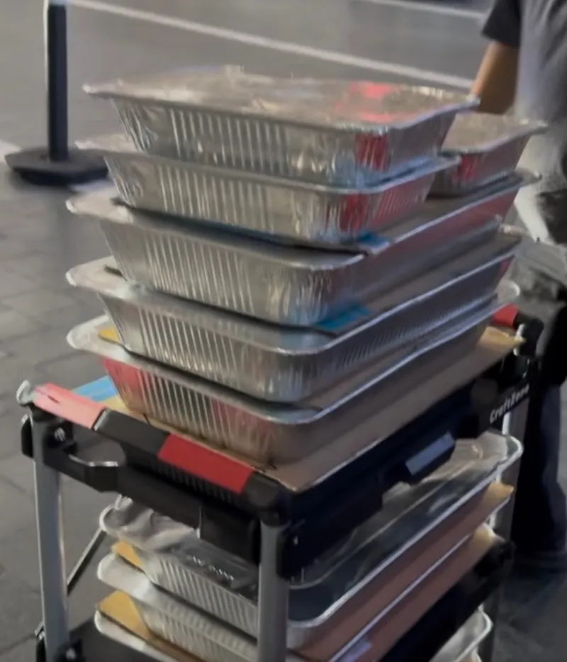 A cart stacked high with foil catering trays on its way to a delivery